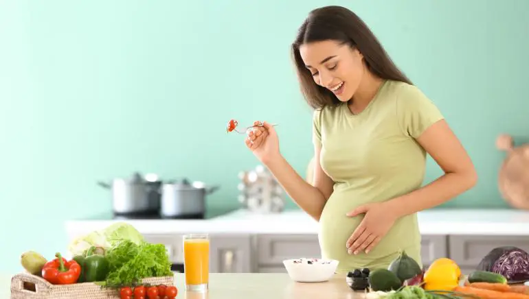 Gambar wanita hamil sedang makan makanan sehat, termasuk buah-buahan