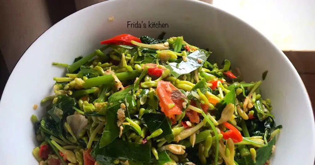 Memasak sayur kangkung bunga pepaya dalam wajan wok